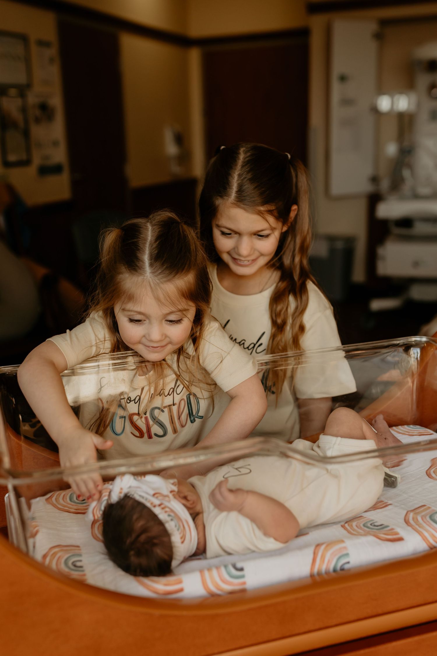 Two people in matching t-shirts caring for an infant on an orange changing table with rainbow pattern padding.