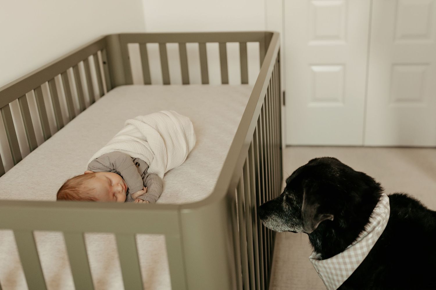 Baby crib decorated with mobile and white bedding set against light colored walls.