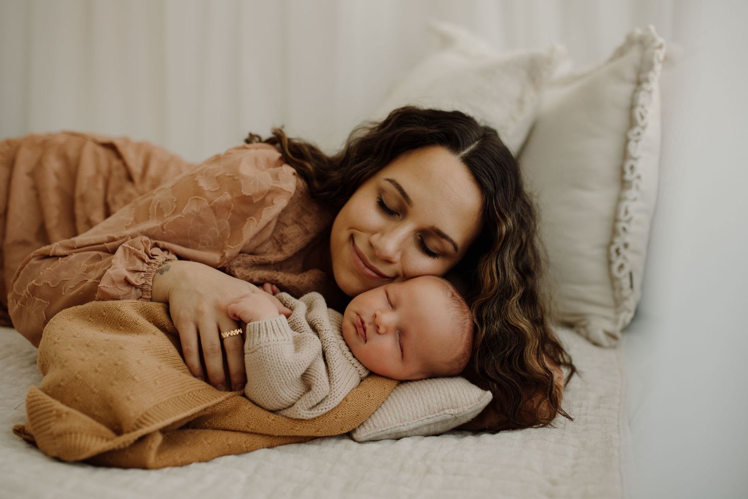 A tender moment of rest and bonding on a cozy bed with soft beige and white linens.