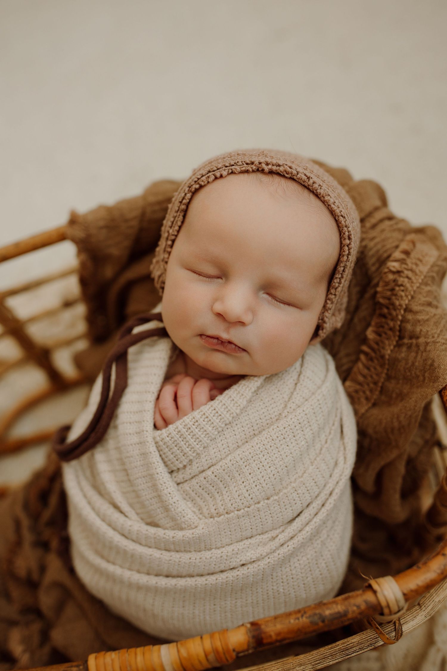 Peaceful sleeping newborn wrapped in cream knit blanket photographed from different angles in sepia tones.