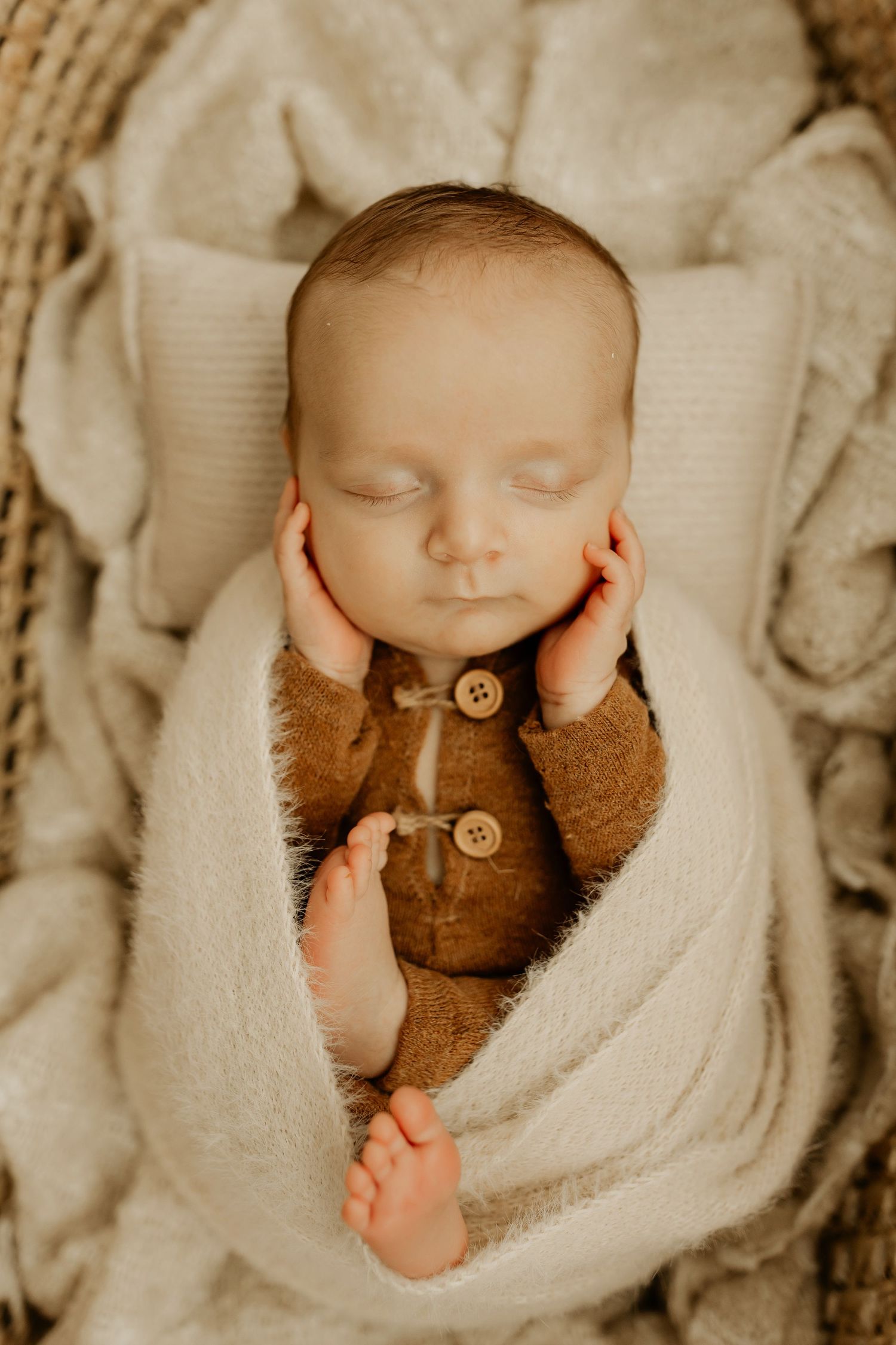 A sleeping newborn baby swaddled in a cream blanket with a brown teddy bear companion.