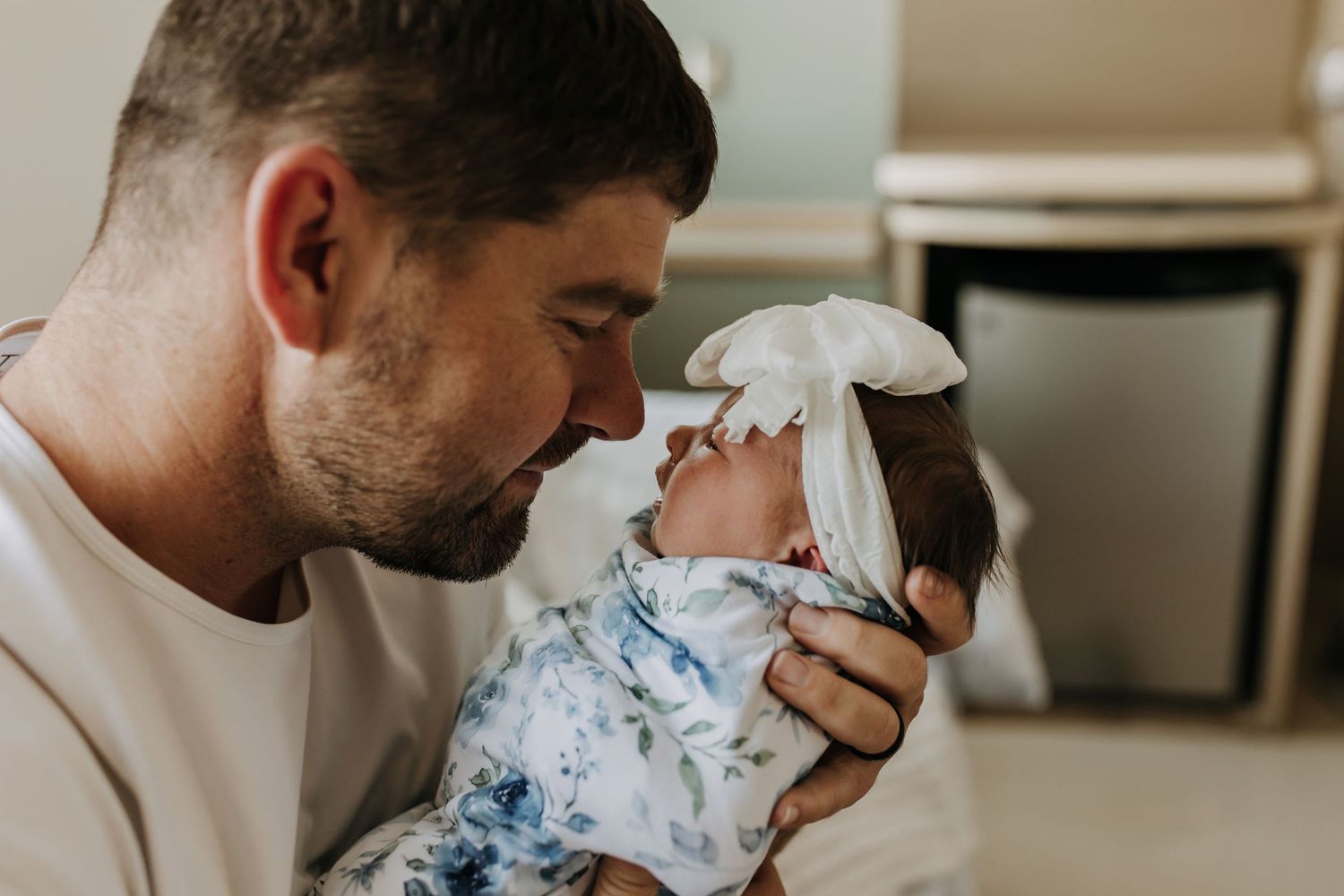 A person holds and snuggles with a small baby wrapped in a floral blanket in a tender moment at home.