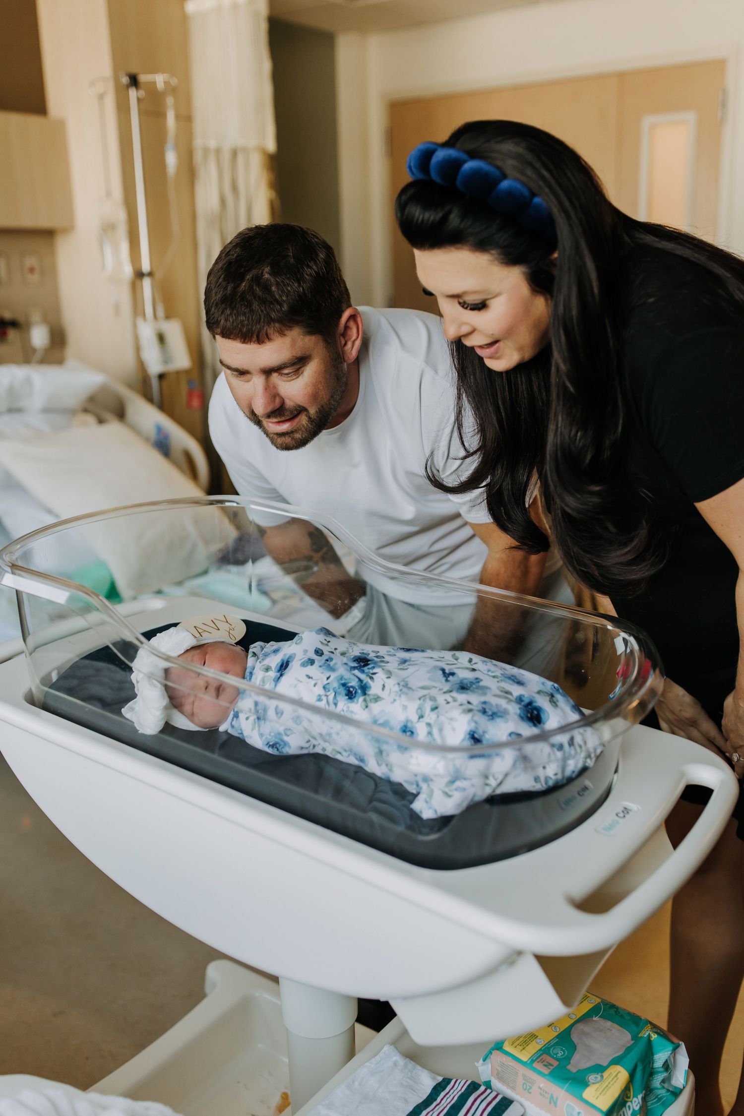 Parents lovingly gaze at their newborn baby resting in a hospital bassinet during first moments together.