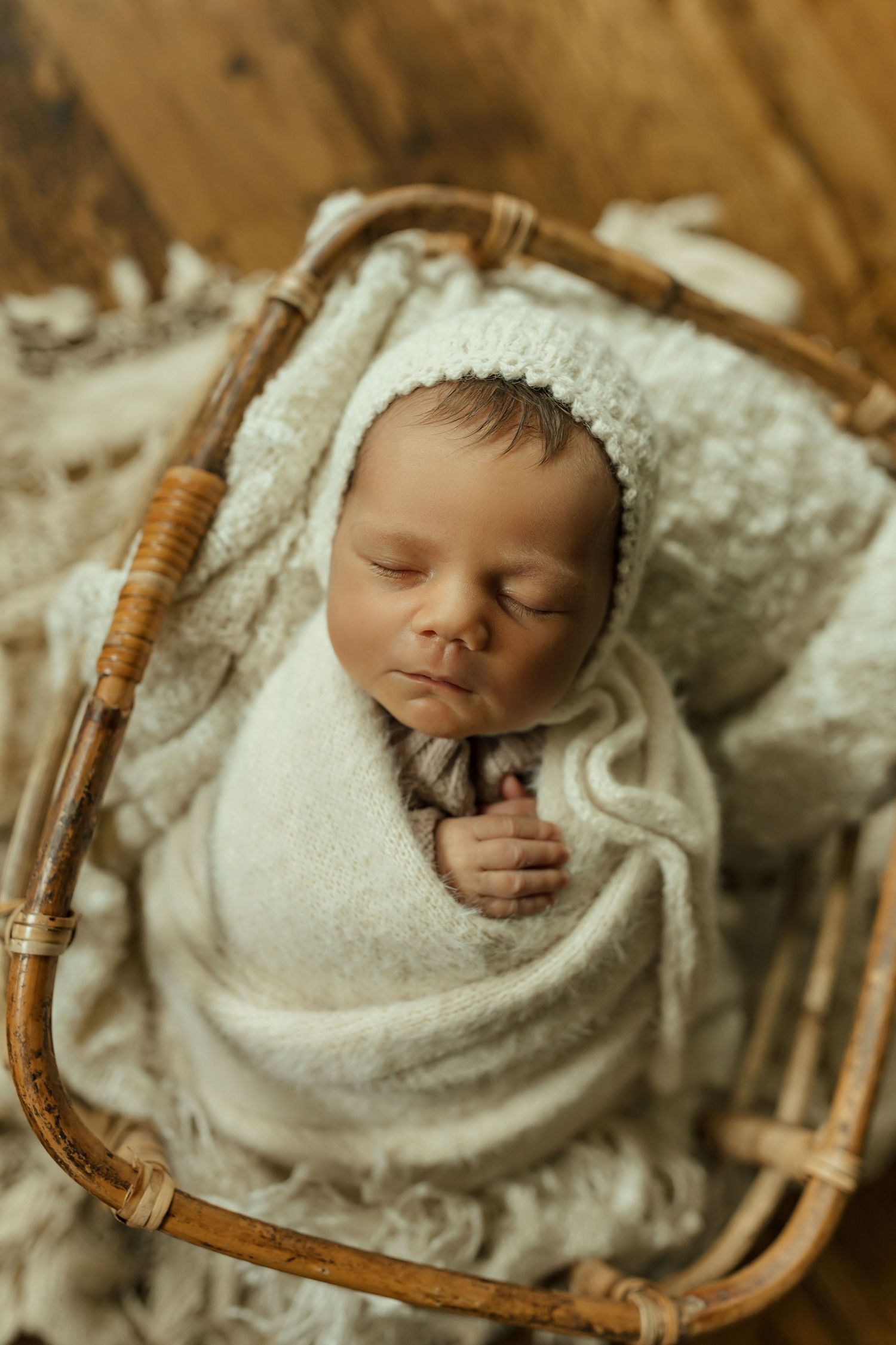 A sleeping newborn baby wrapped in white swaddling cloth lies peacefully in a brown wicker basket.