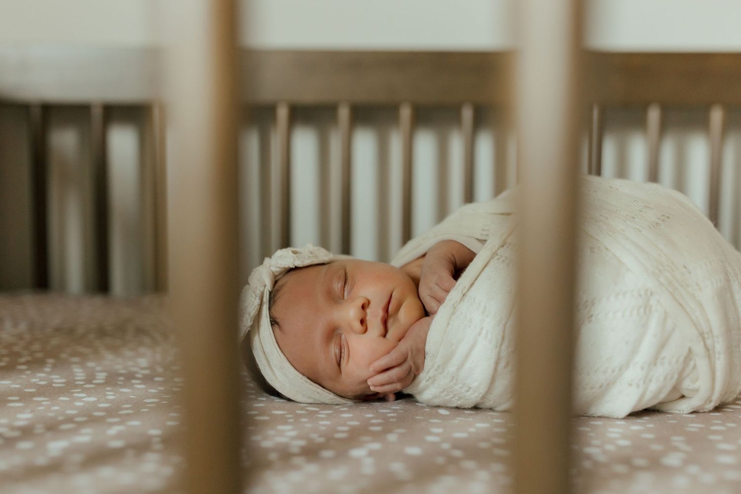 A sleeping baby in white clothing rests peacefully inside a wooden crib.