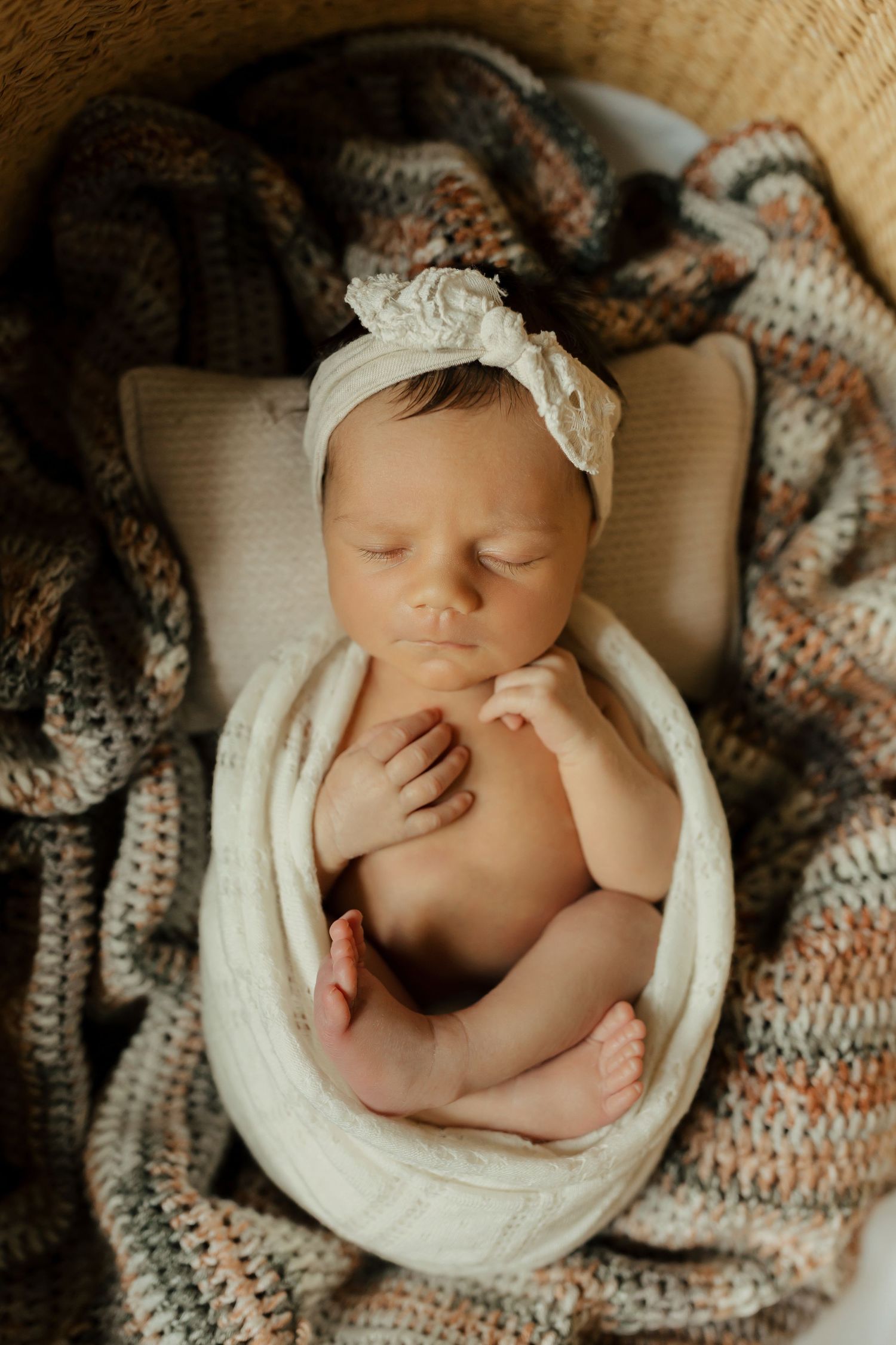 A sleeping newborn baby wrapped in white fabric nestled in a cozy brown and white knitted blanket.