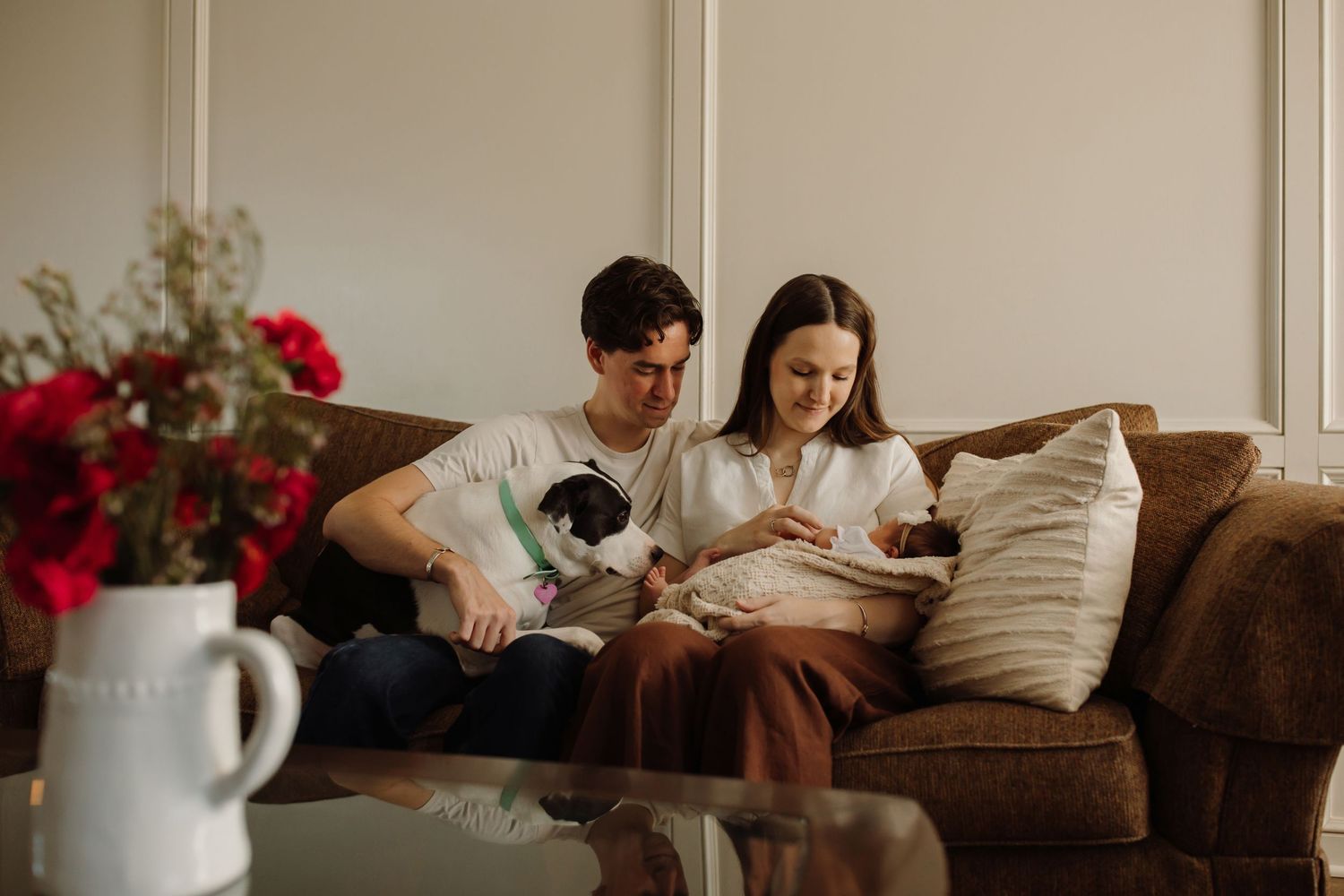 A couple relaxes on a brown leather couch while using digital devices in a cozy living room setting.