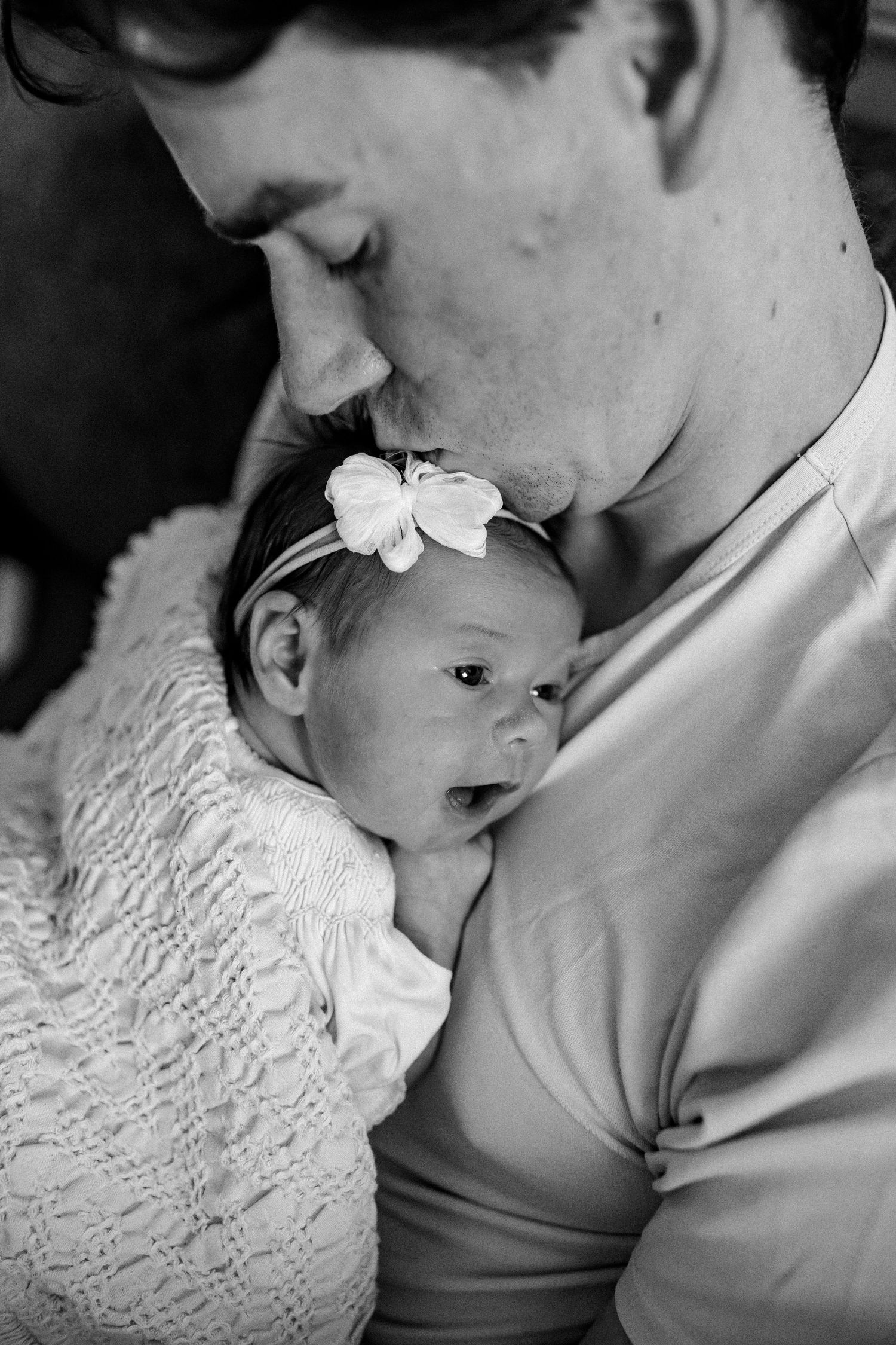 A tender black and white photo series showing intimate moments between a parent and newborn baby in white lace clothing.