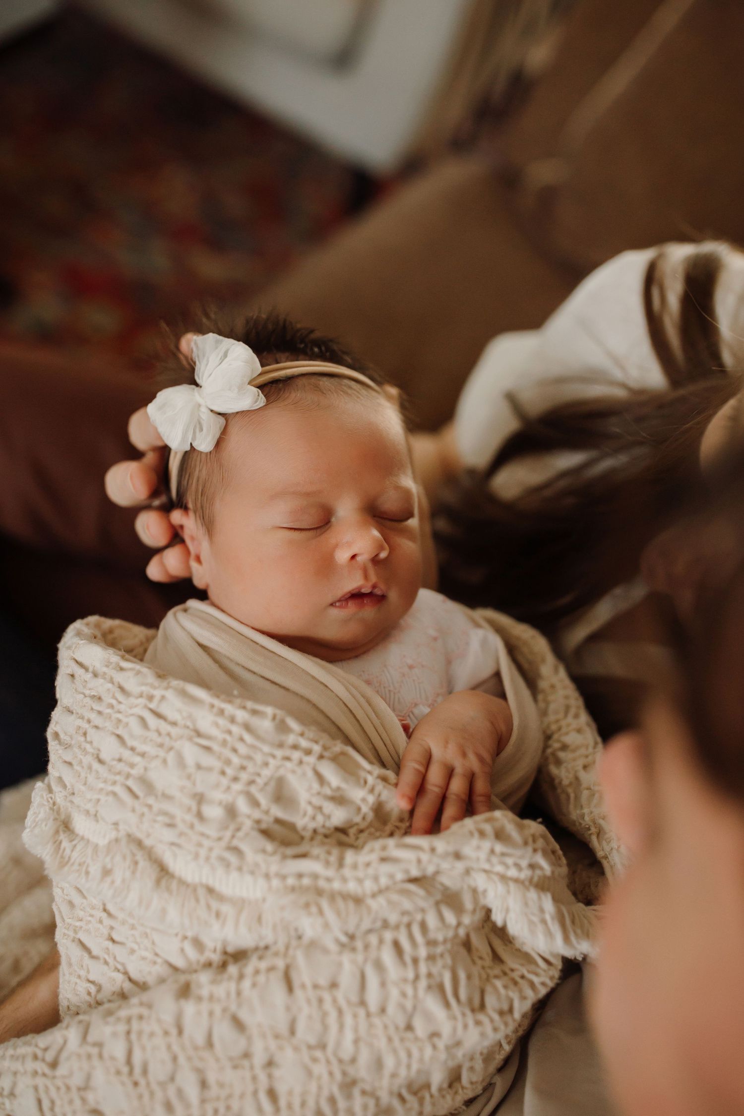 Sleeping newborn baby wrapped in cream lace blanket with white bow headband in natural light portrait series.