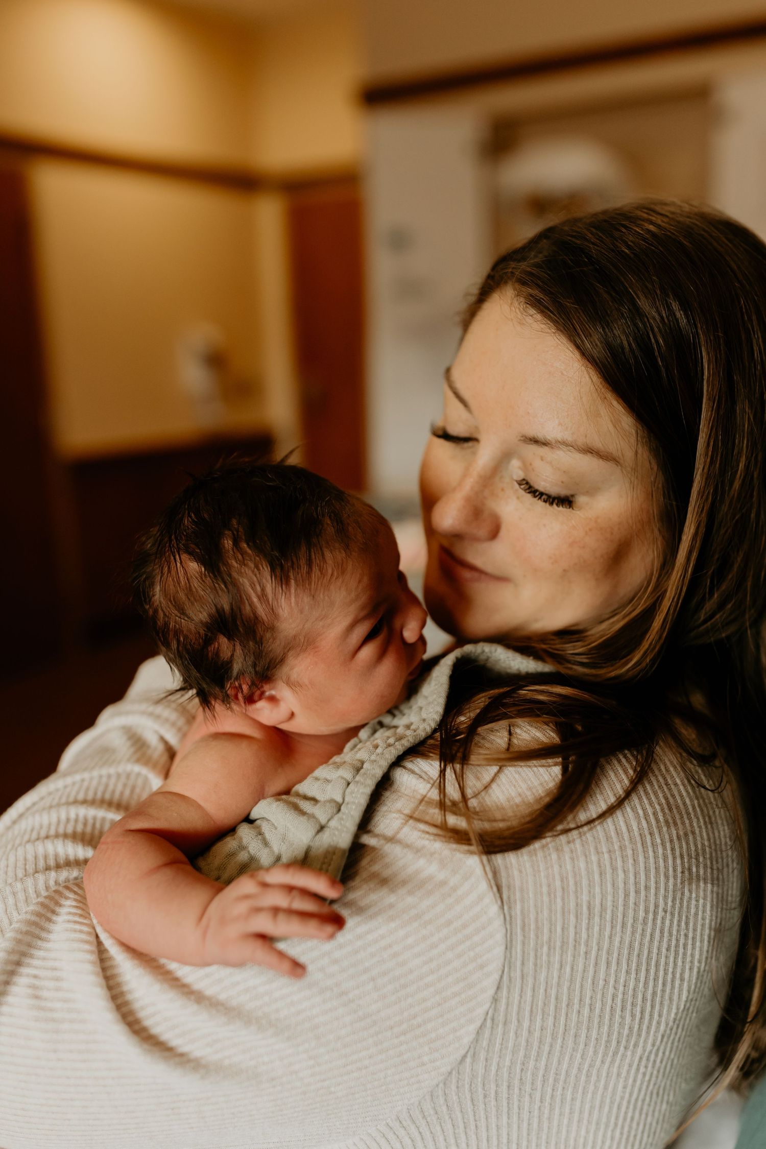A tender moment between mother and newborn baby in warm lighting as they share a gentle embrace.