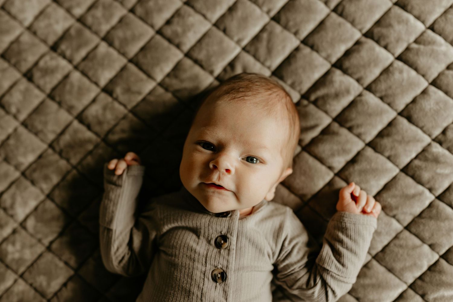 Six connected photos show a baby wearing a gray quilted onesie lying on quilted fabric in varying poses.