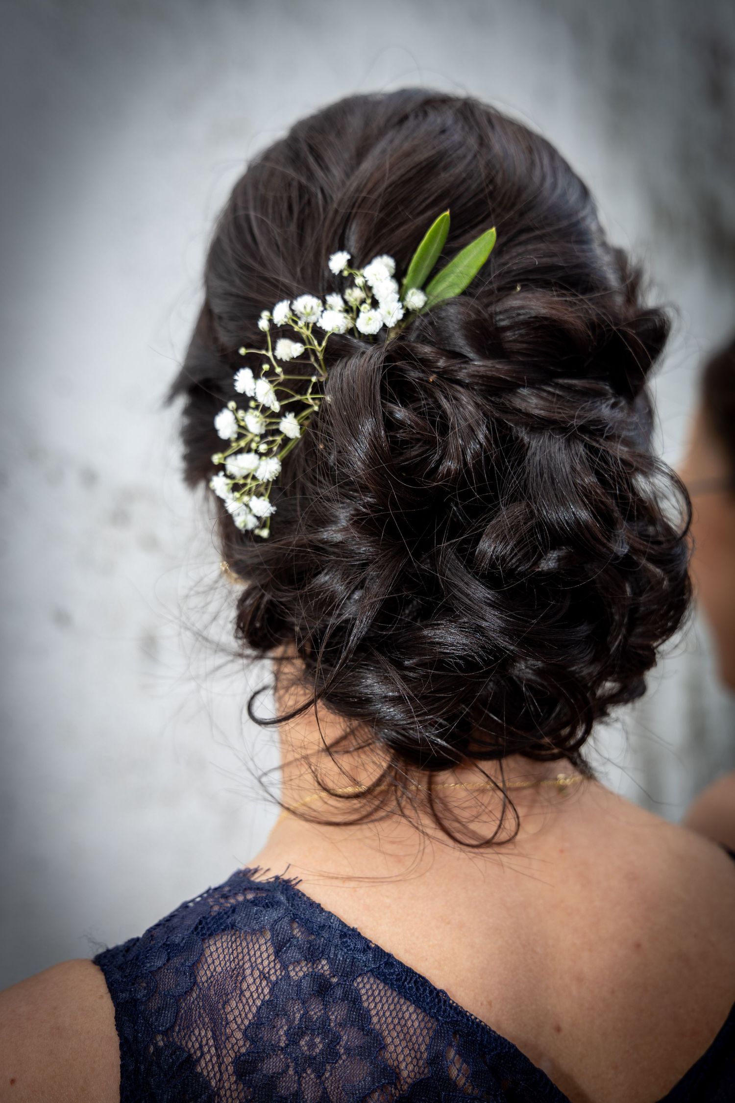 Dark-haired woman with elegant updo adorned with delicate white baby's breath flowers at wedding.