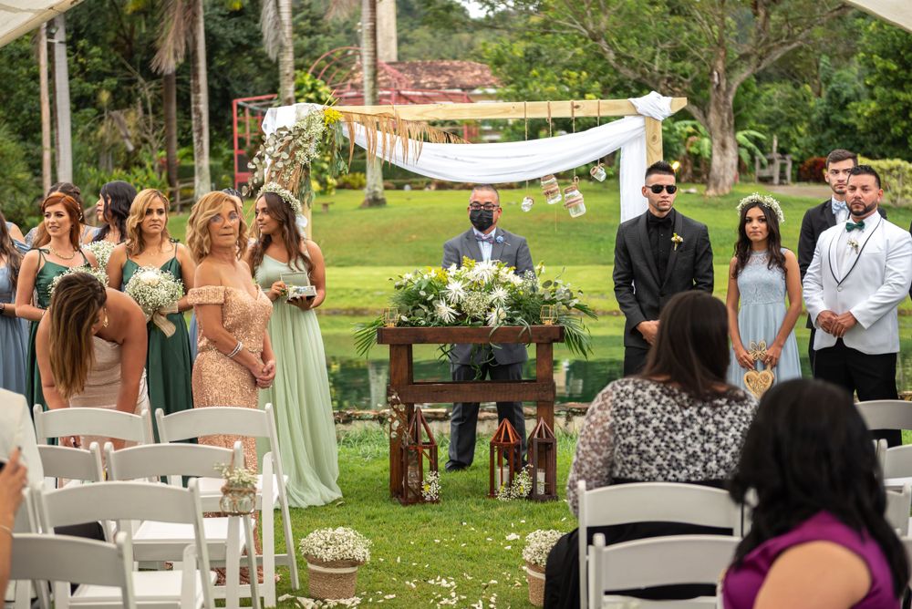 Outdoor garden wedding ceremony with guests seated in white chairs and sage green bridesmaid dresses.
