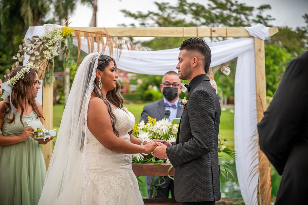 Outdoor wedding ceremony under white fabric arch with couple exchanging vows.