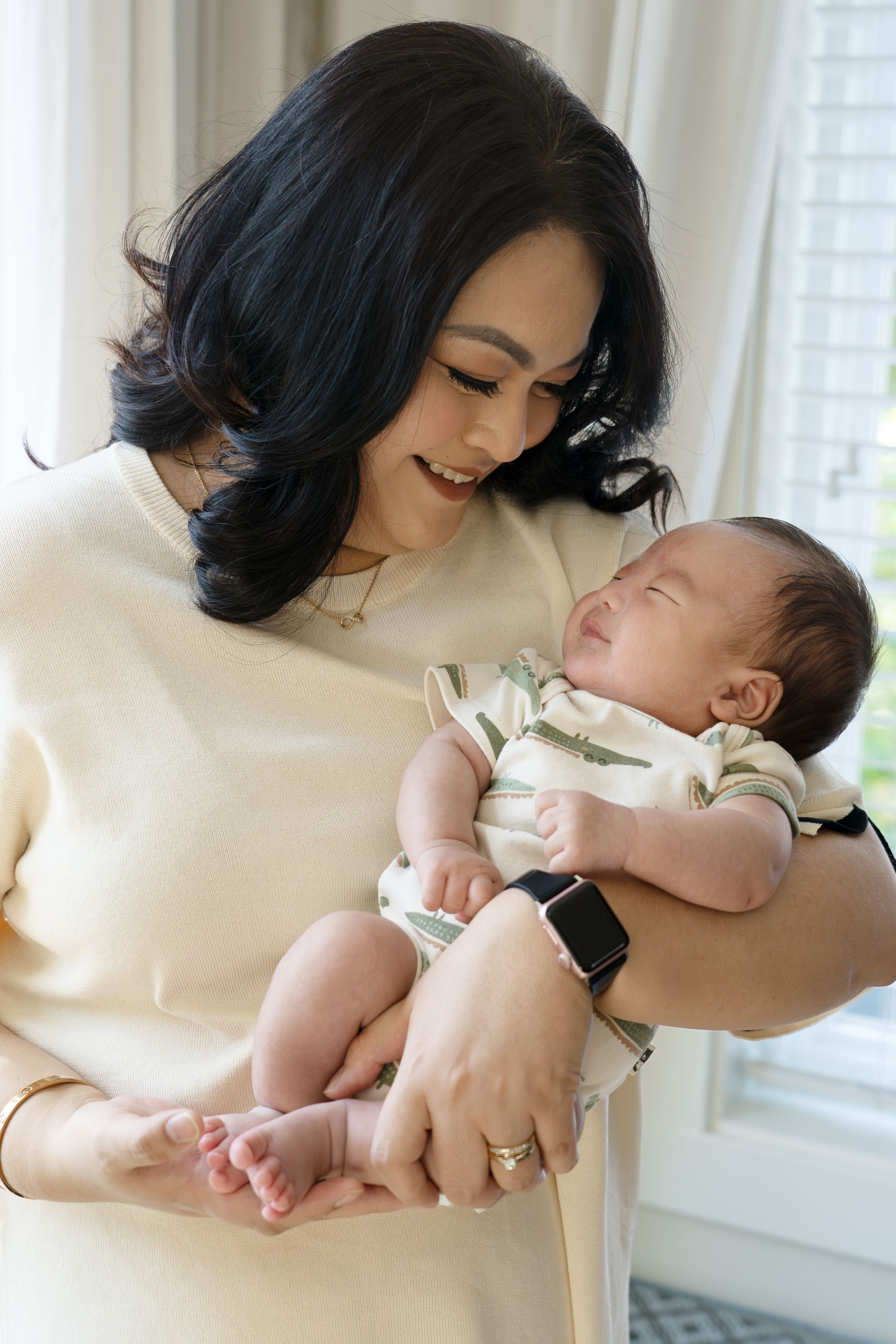 A tender moment as a parent in cream sweater holds sleeping newborn baby.