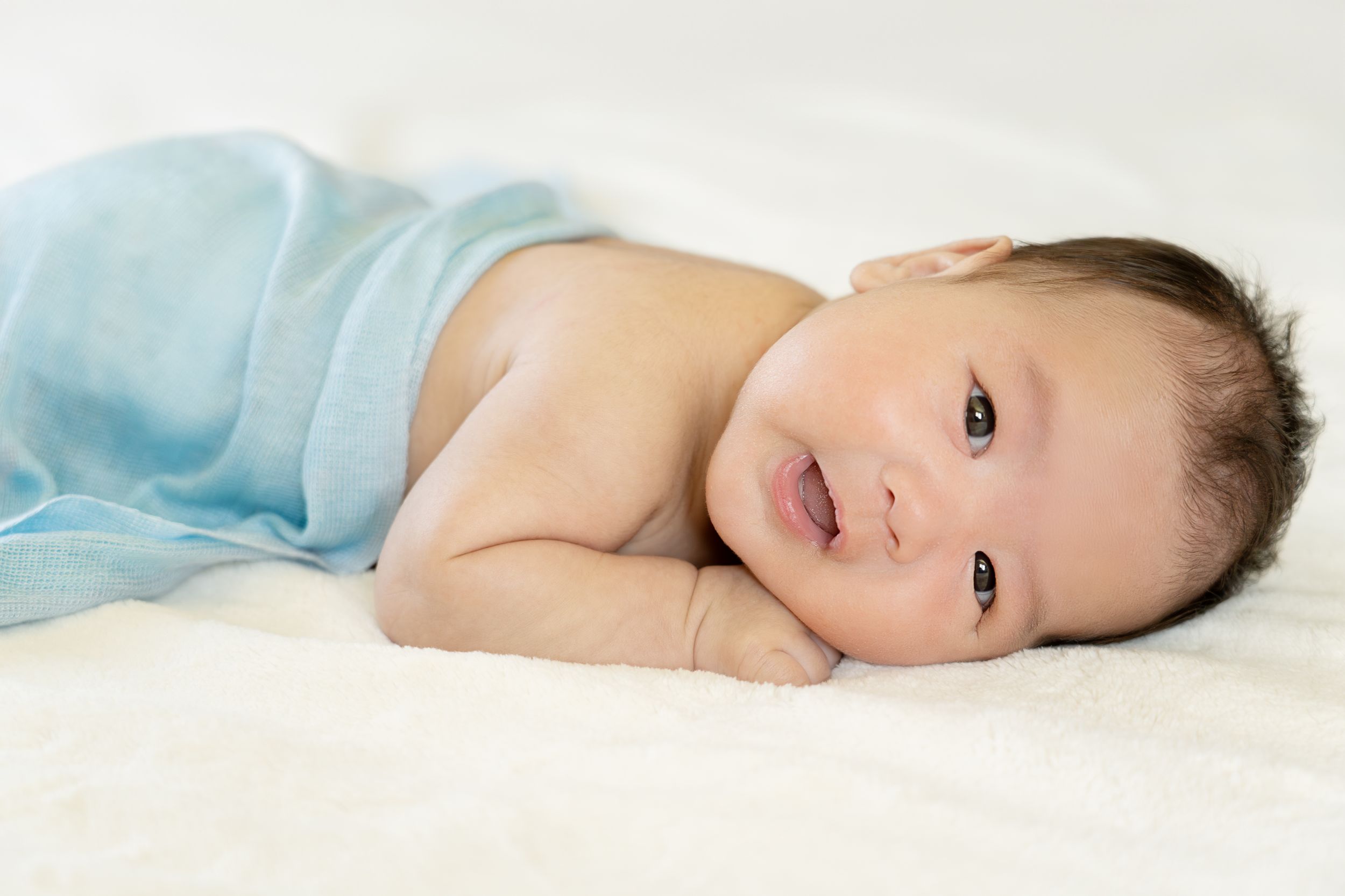 Peaceful baby in light blue swaddle lying on white bedding.