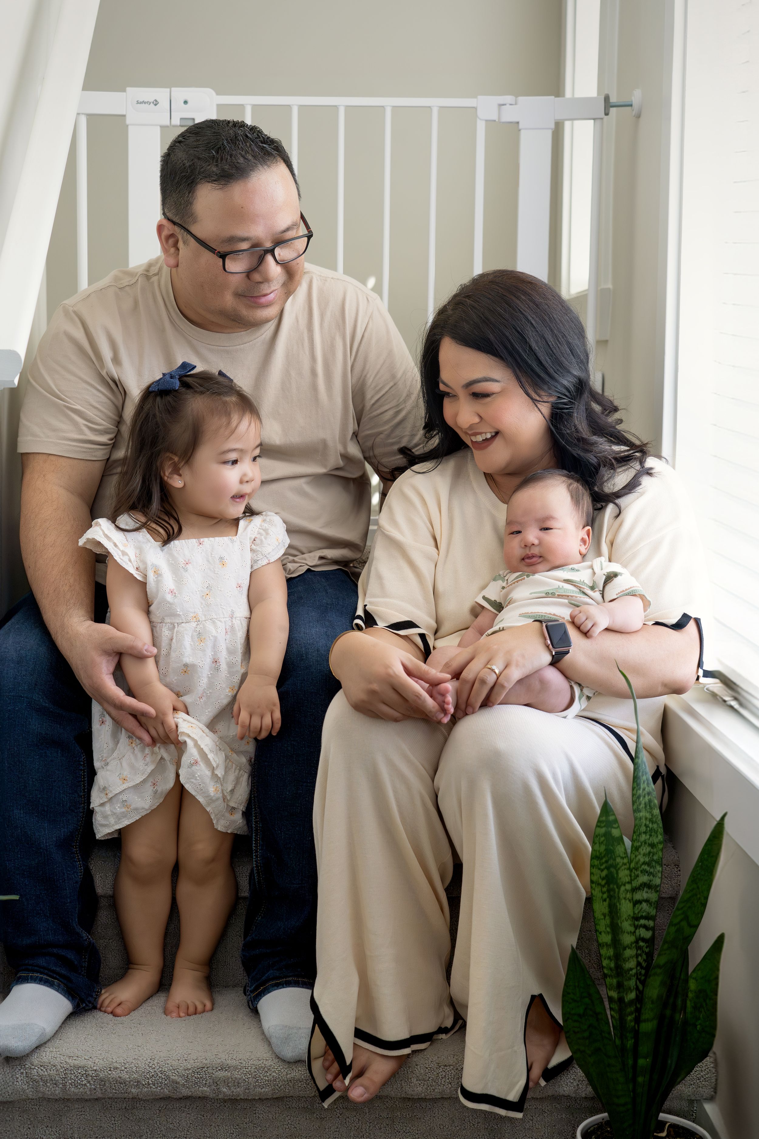 Family sitting together by window with houseplant, sharing tender moment.