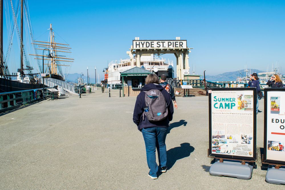 Tourist walking along Fisherman's Wharf pier with signs and boats in view.