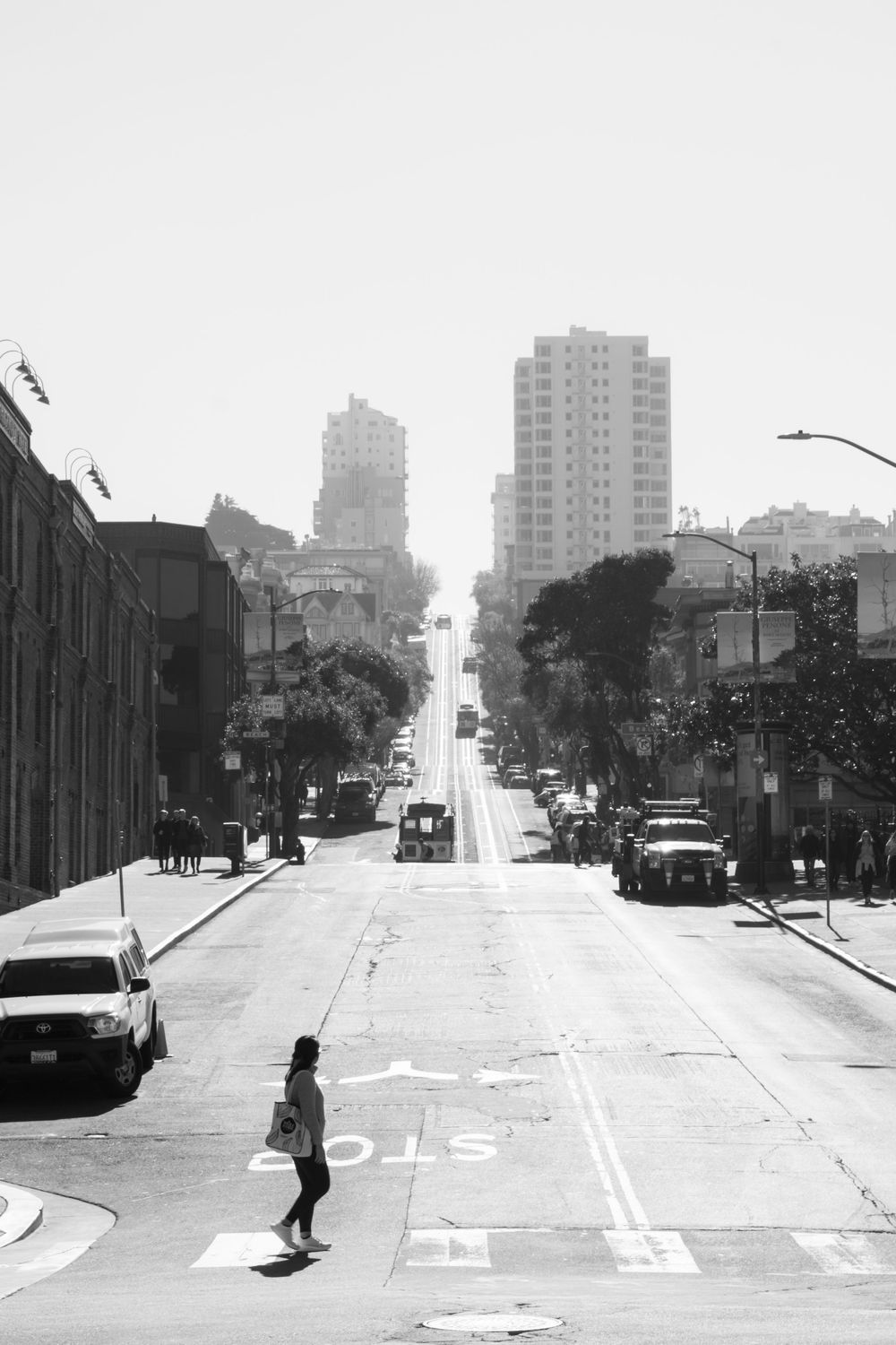 A steep San Francisco street with high-rise buildings and parked cars in black and white.