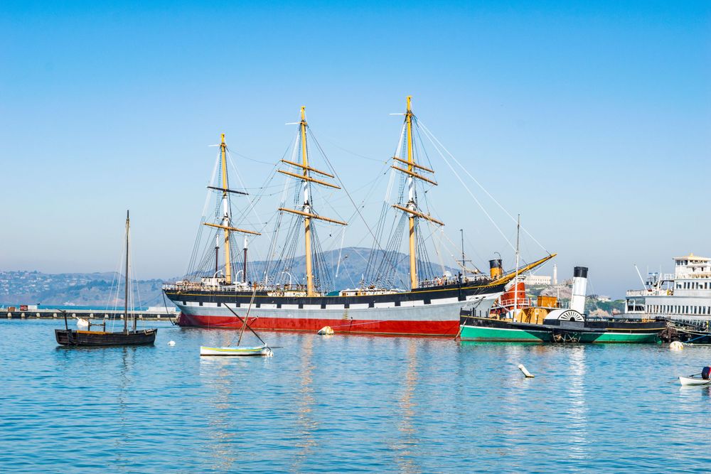 Historic sailing vessels moored at Fisherman's Wharf with the San Francisco skyline in the distance.