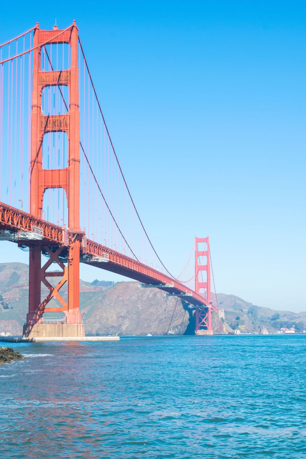 A vibrant orange Golden Gate Bridge stretches across turquoise waters under clear blue skies.