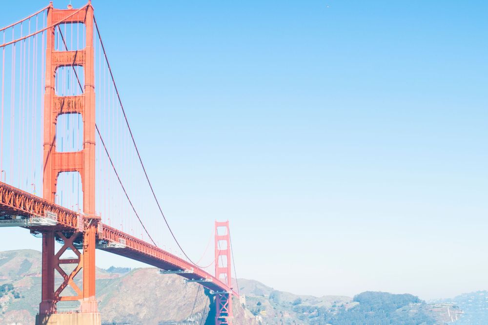 The Golden Gate Bridge stands majestically against a bright blue sky with mountains in the background.