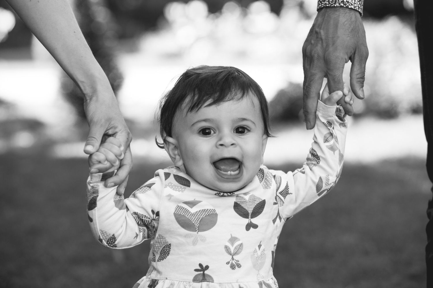 Photo noir et blanc d'une jeune enfant qui sourit en tenant les mains de ses parents