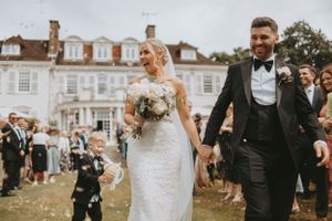 Joyful outdoor wedding celebration with guests throwing confetti in front of classic building.
