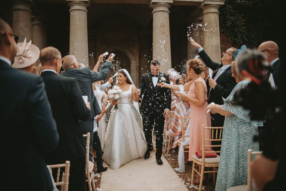 Wedding guests celebrating at an elegant venue with columns and wooden chairs.