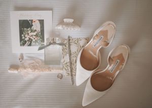 Wedding accessories including white heels and delicate decor arranged on light background.