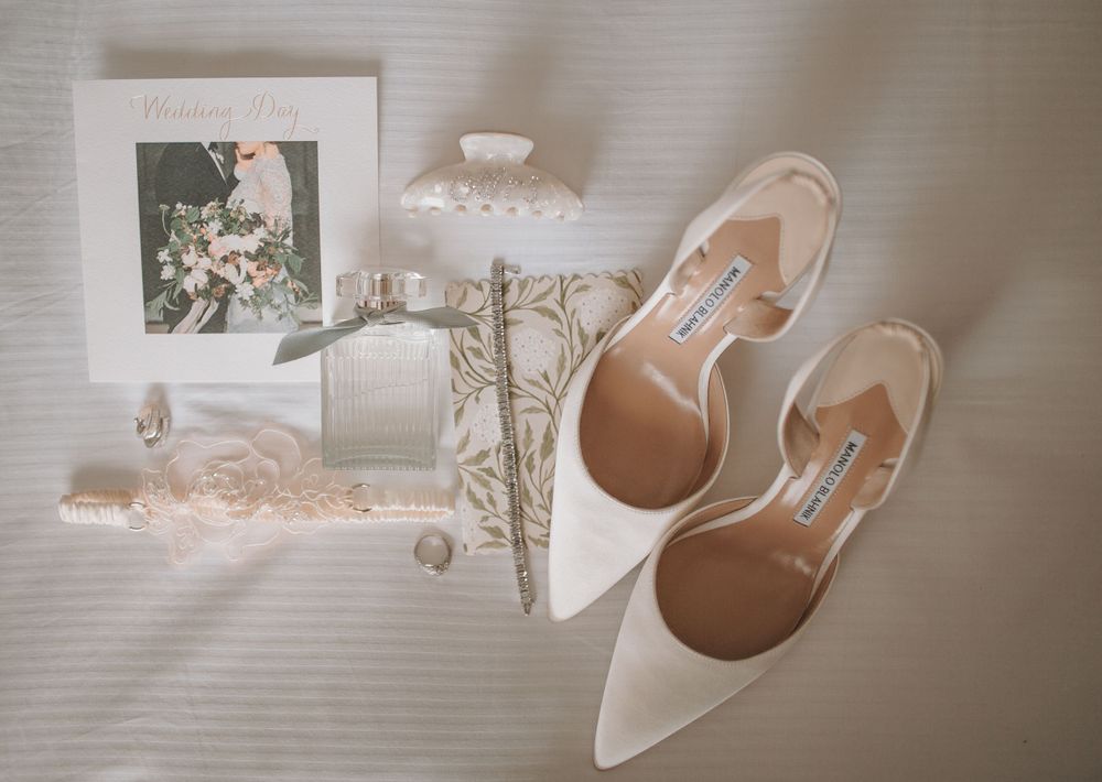 Wedding accessories including white heels and delicate decor arranged on light background.