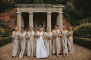 Wedding party lineup with bridesmaids in matching taupe dresses beside classical columns.
