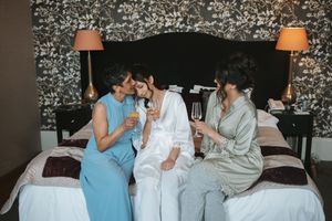Bridesmaids in blue and gray robes laughing together during wedding preparations.