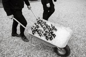 Wedding staff transport supplies using wheelbarrows on a gravel path.