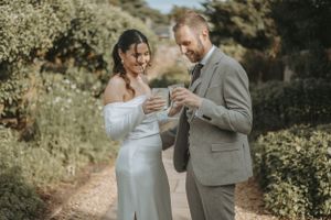 Romantic outdoor wedding photoshoot showing couple in white dress and gray suit against natural greenery backdrop.