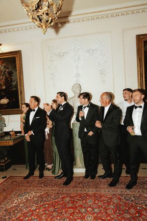 Wedding guests in formal attire laughing and celebrating inside a grand ornate reception venue.