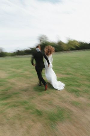 A blurred motion shot of a bride and groom running across a green field on their wedding day.