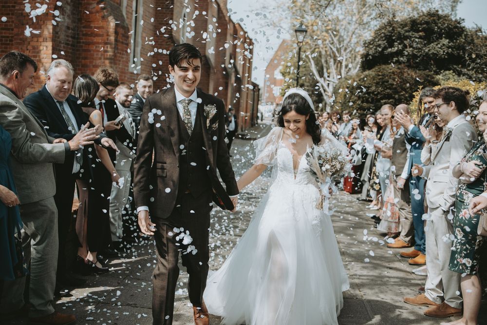 Wedding couple walks through shower of confetti with guests lining pathway.