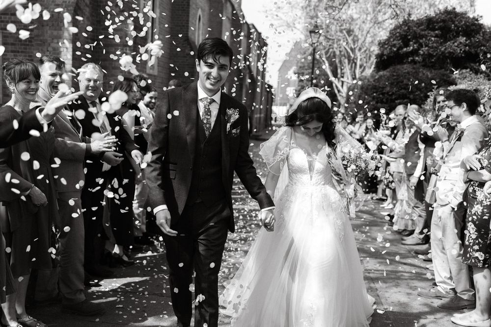 Black and white photo of newlyweds walking through confetti shower after ceremony.