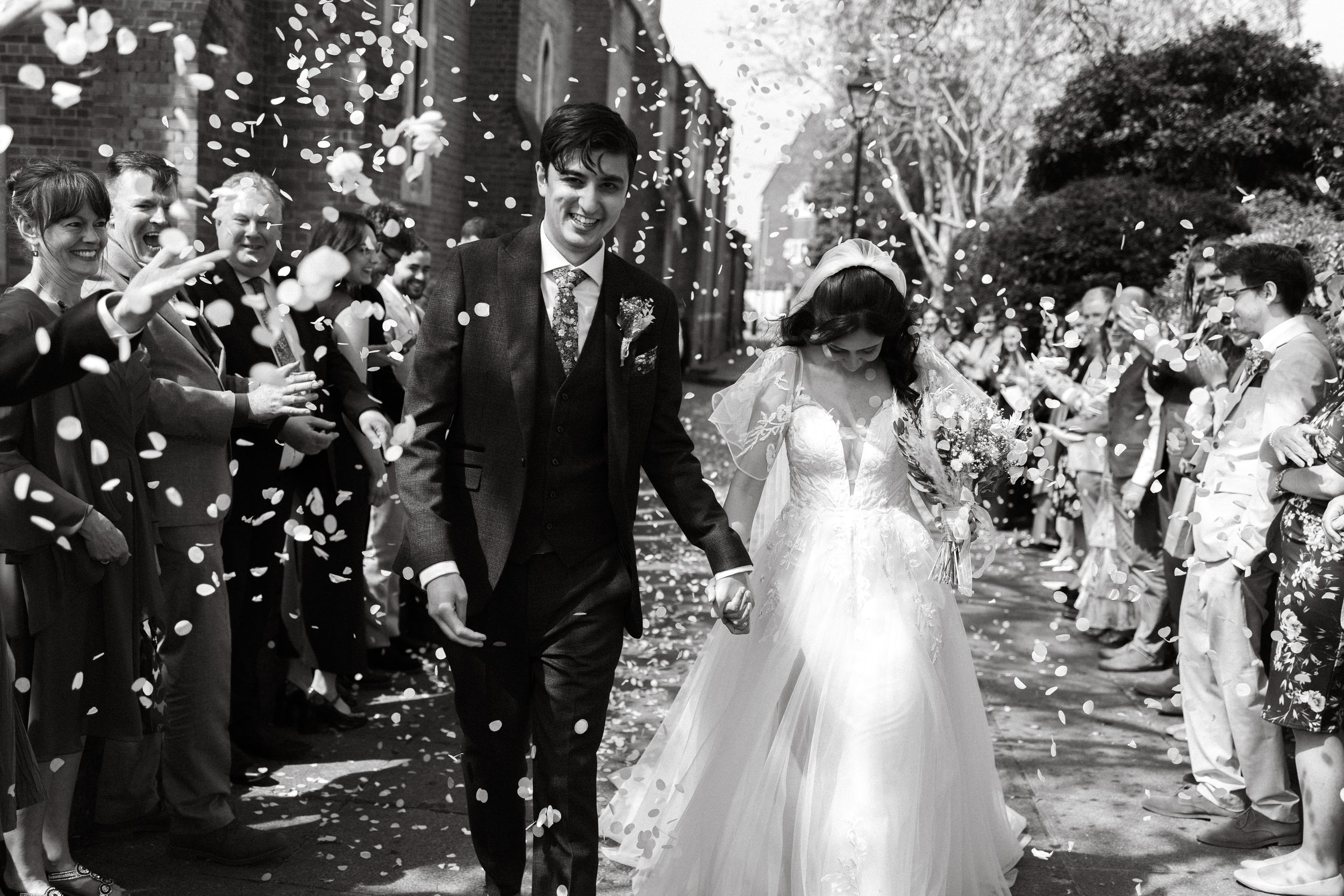 Black and white photo of newlyweds walking through confetti shower after ceremony.