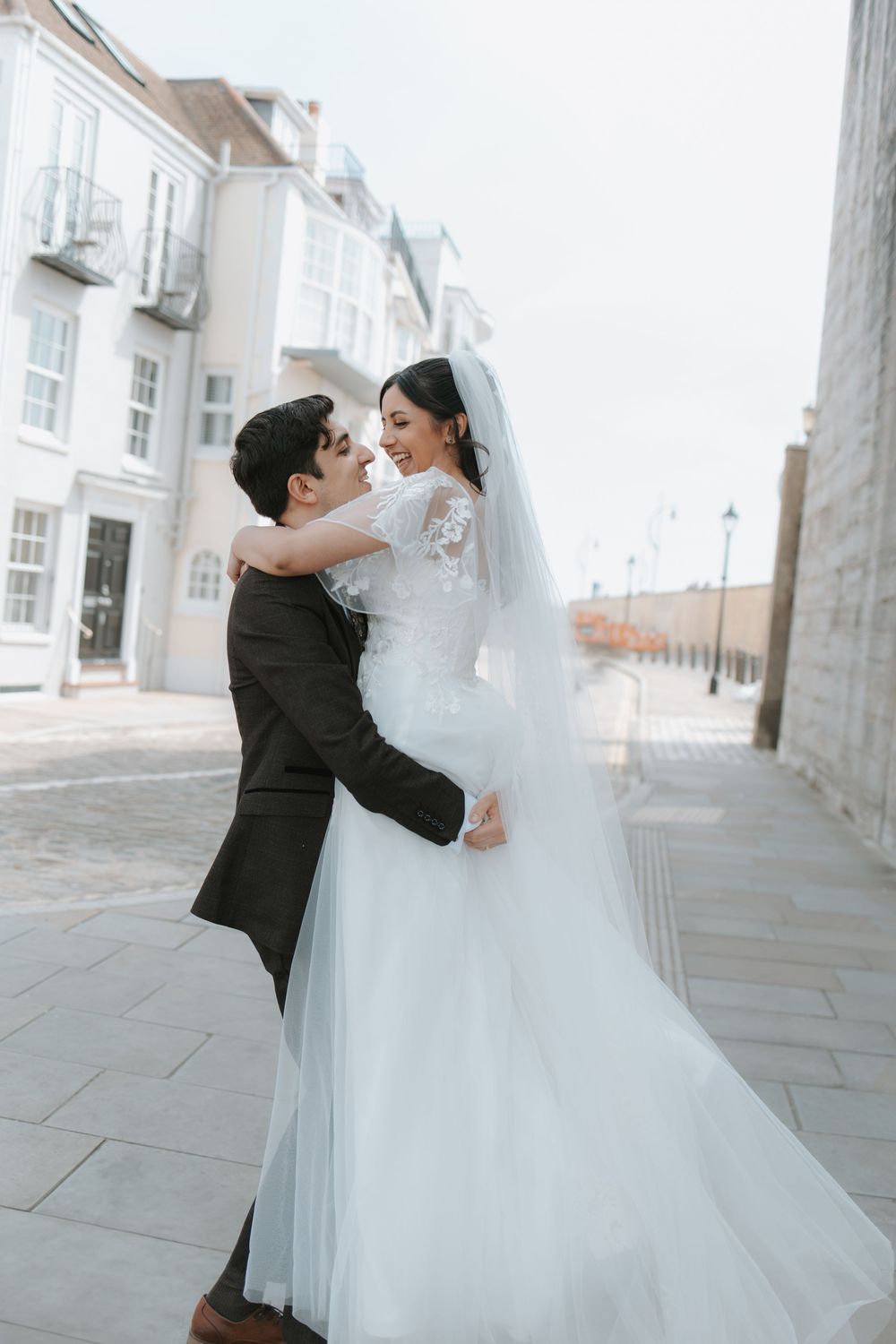 Romantic moment between newlyweds on cobblestone street with white buildings.