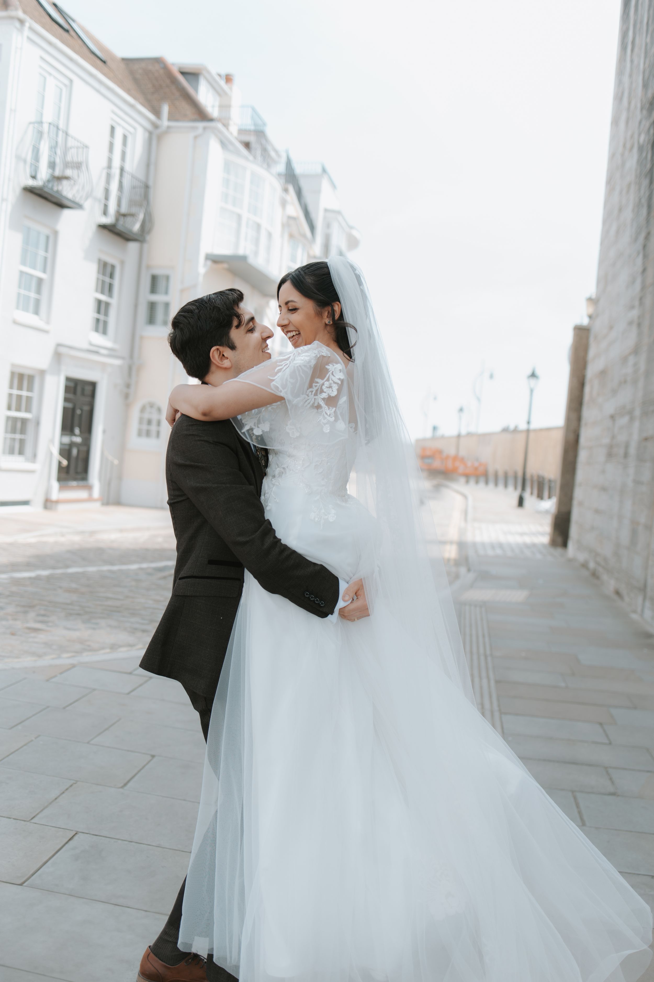 Romantic moment between newlyweds on cobblestone street with white buildings.