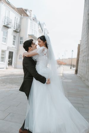 Romantic moment between newlyweds on cobblestone street with white buildings.