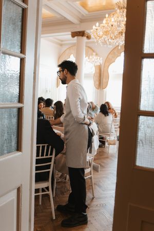 Interior of an elegant white room with crystal chandeliers and natural light streaming through windows.