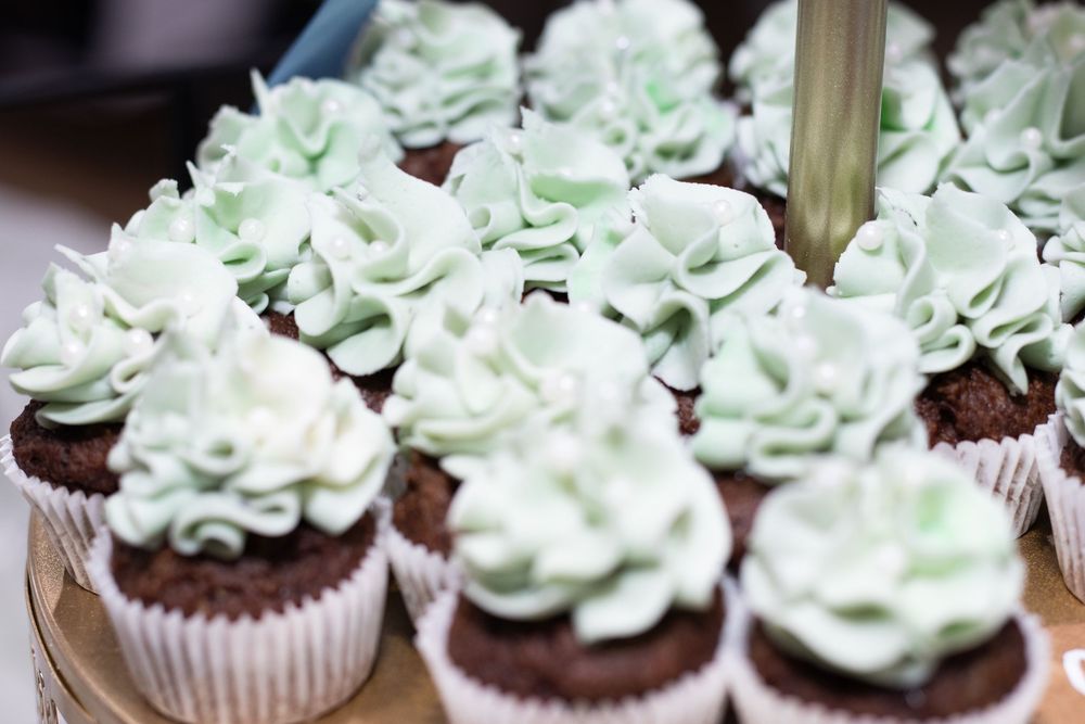 Chocolate cupcakes topped with swirls of light green mint frosting arranged in rows on a display.
