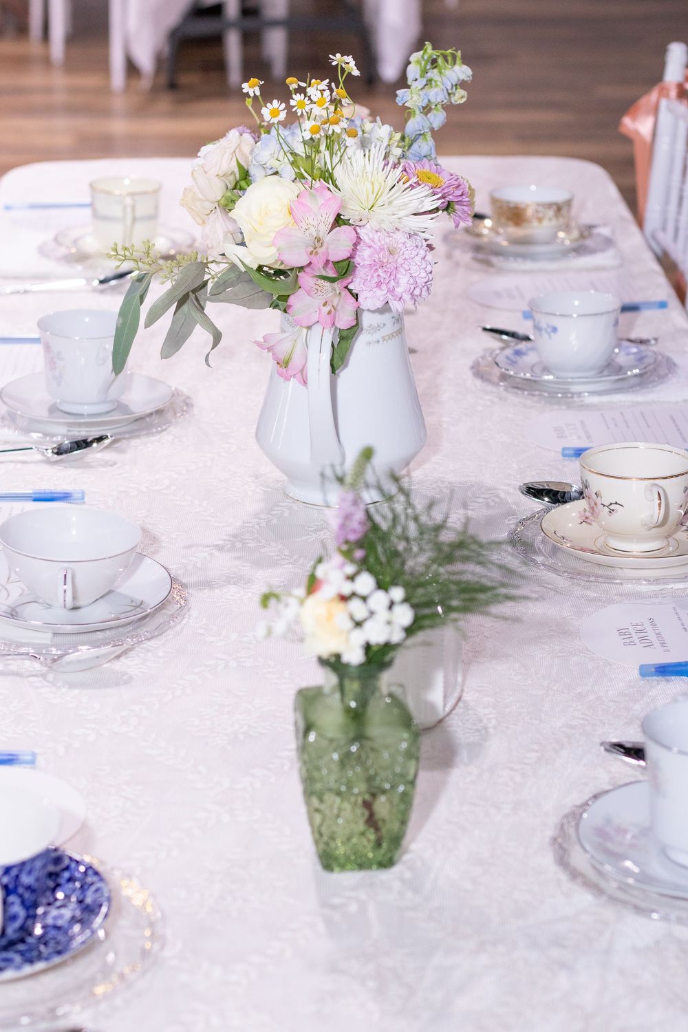 Elegant table settings with white teacups and delicate floral centerpieces in glass vases on a white tablecloth.