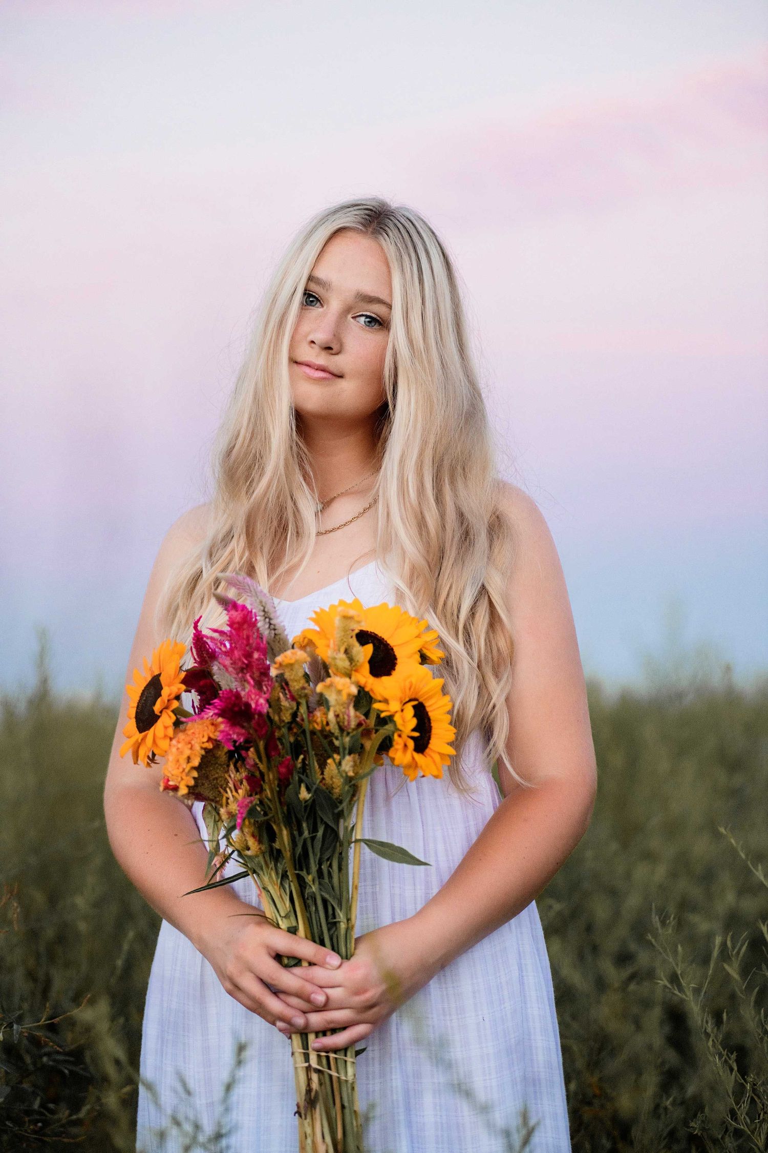 A summery portrait with someone holding a vibrant bouquet of sunflowers and wildflowers in a field.