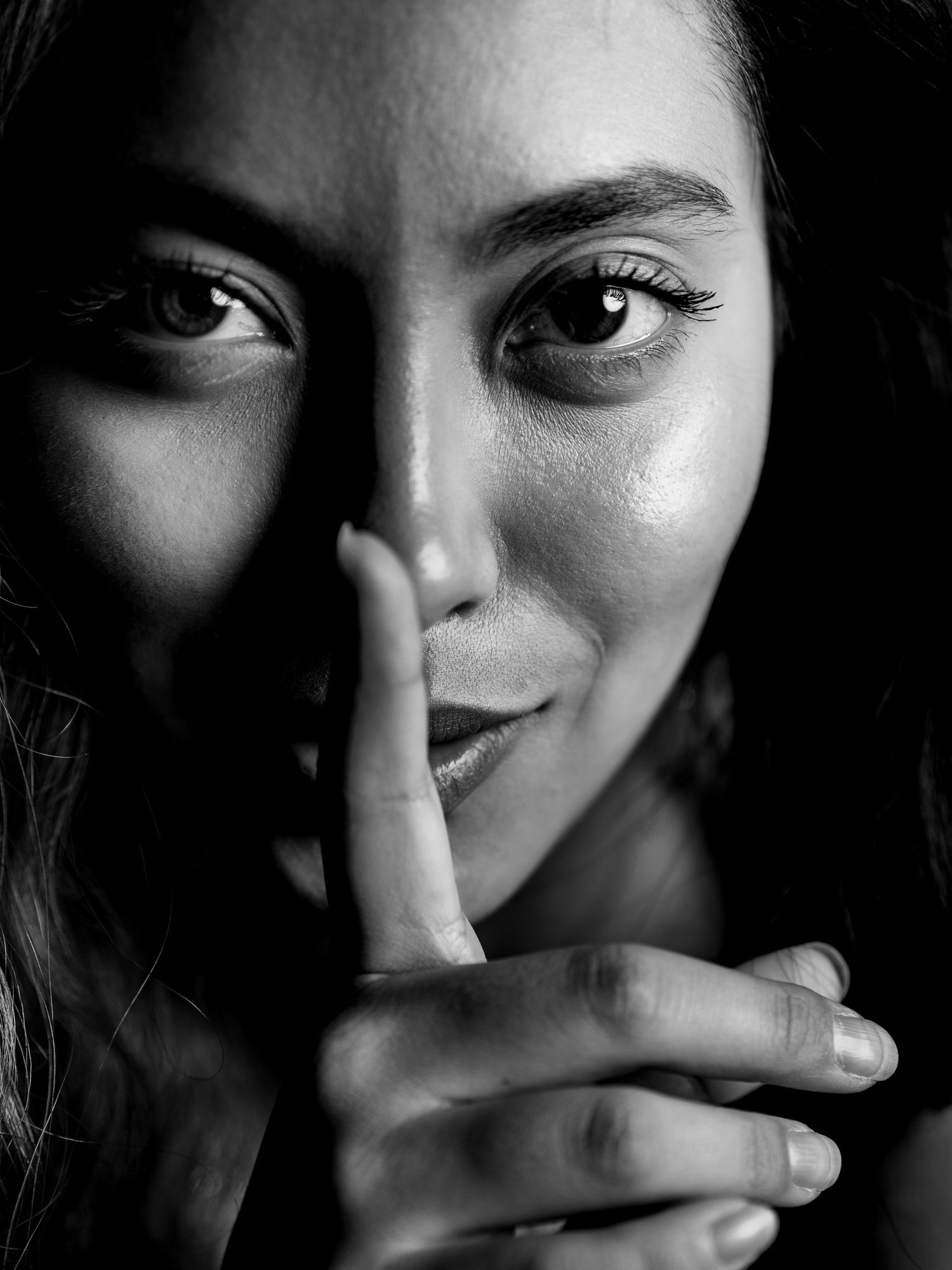 Black and white portrait of a woman making a shush gesture with finger to lips.