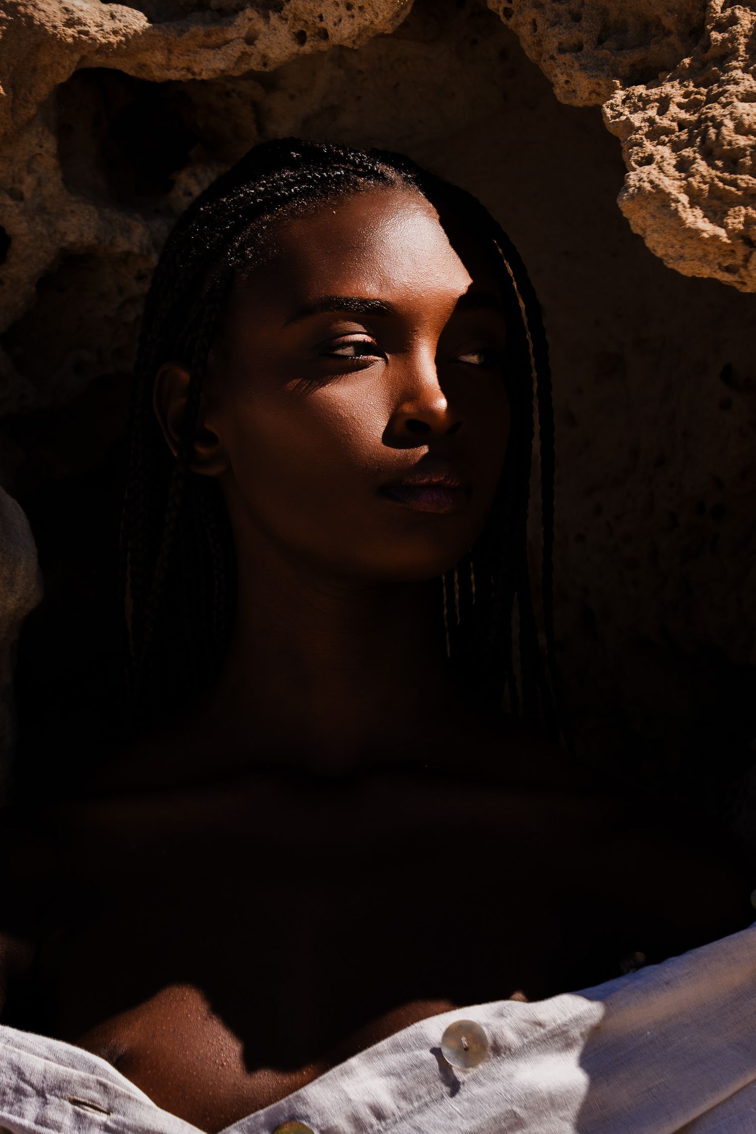 Young woman with braided hair in dramatic shadow and sunlight near stone wall.