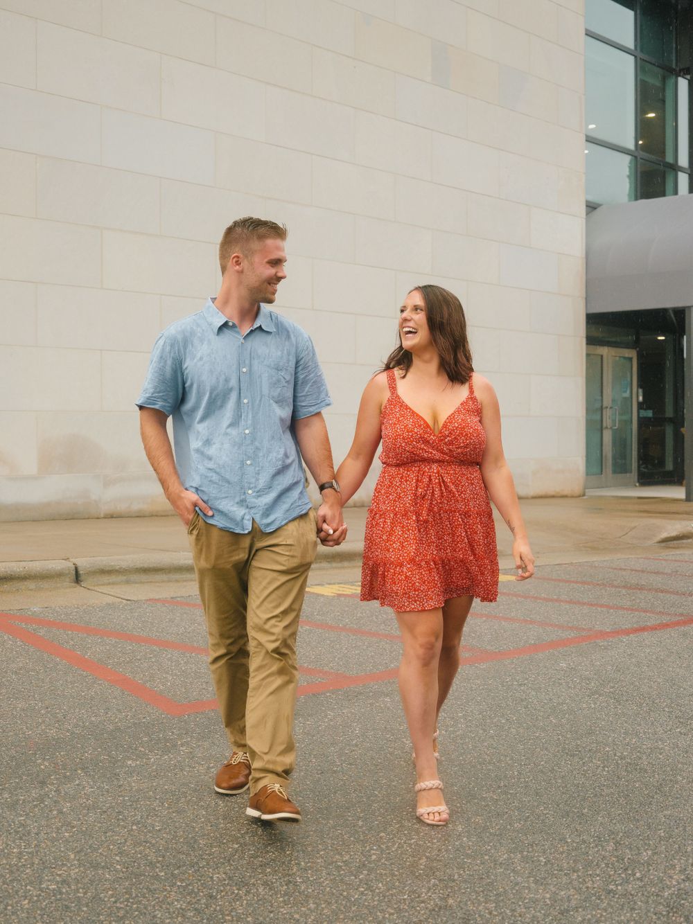 A couple walking hand in hand on a sidewalk, wearing casual summer outfits.